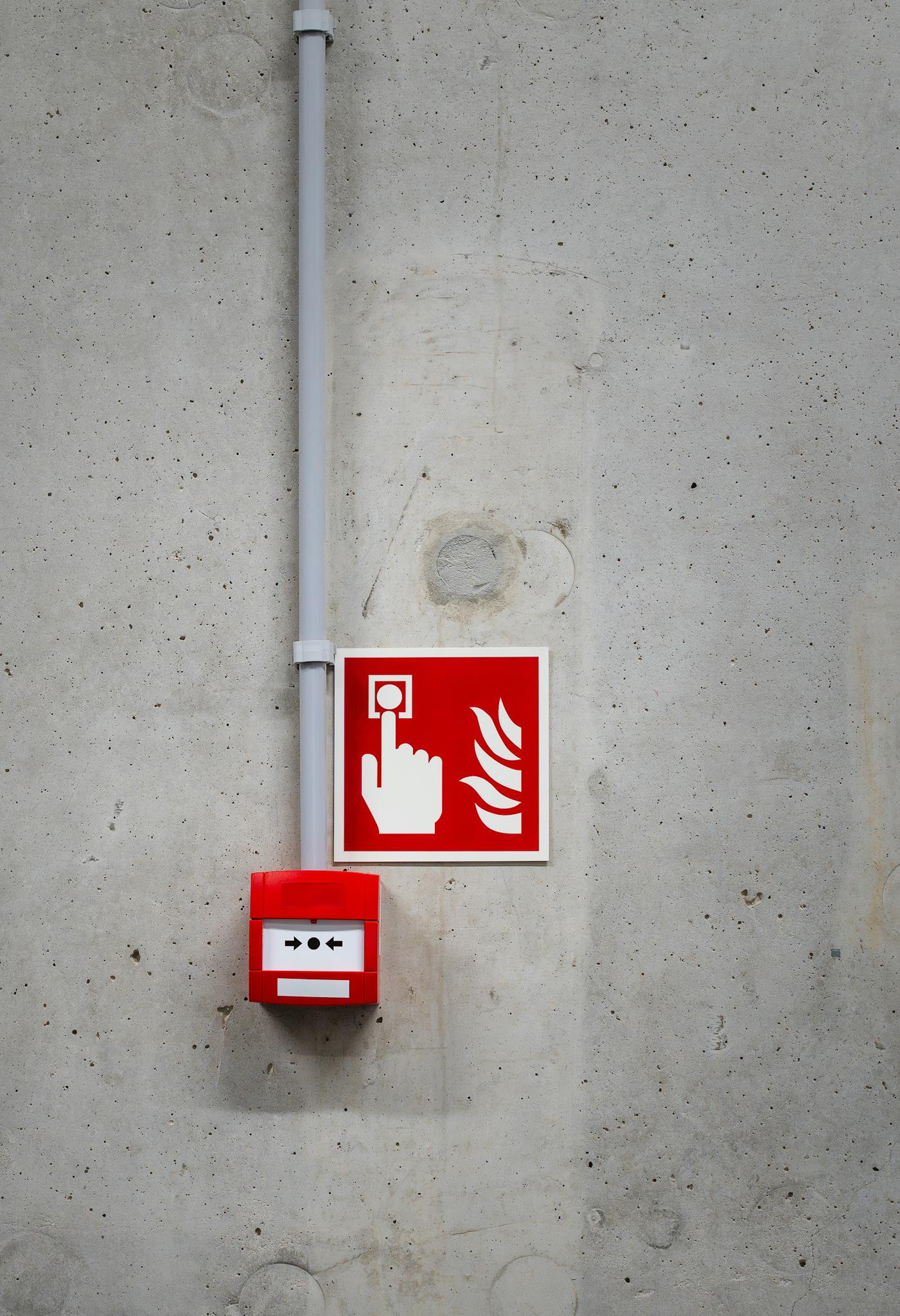 A red fire alarm switch with a warning sign on a concrete wall, highlighting safety in industrial settings.